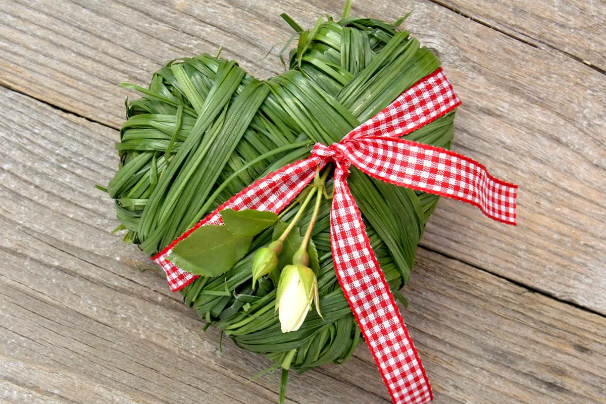 Aus Grashalmen geformtes Herz mit einer roten Schleife und weißen Blüten verziert