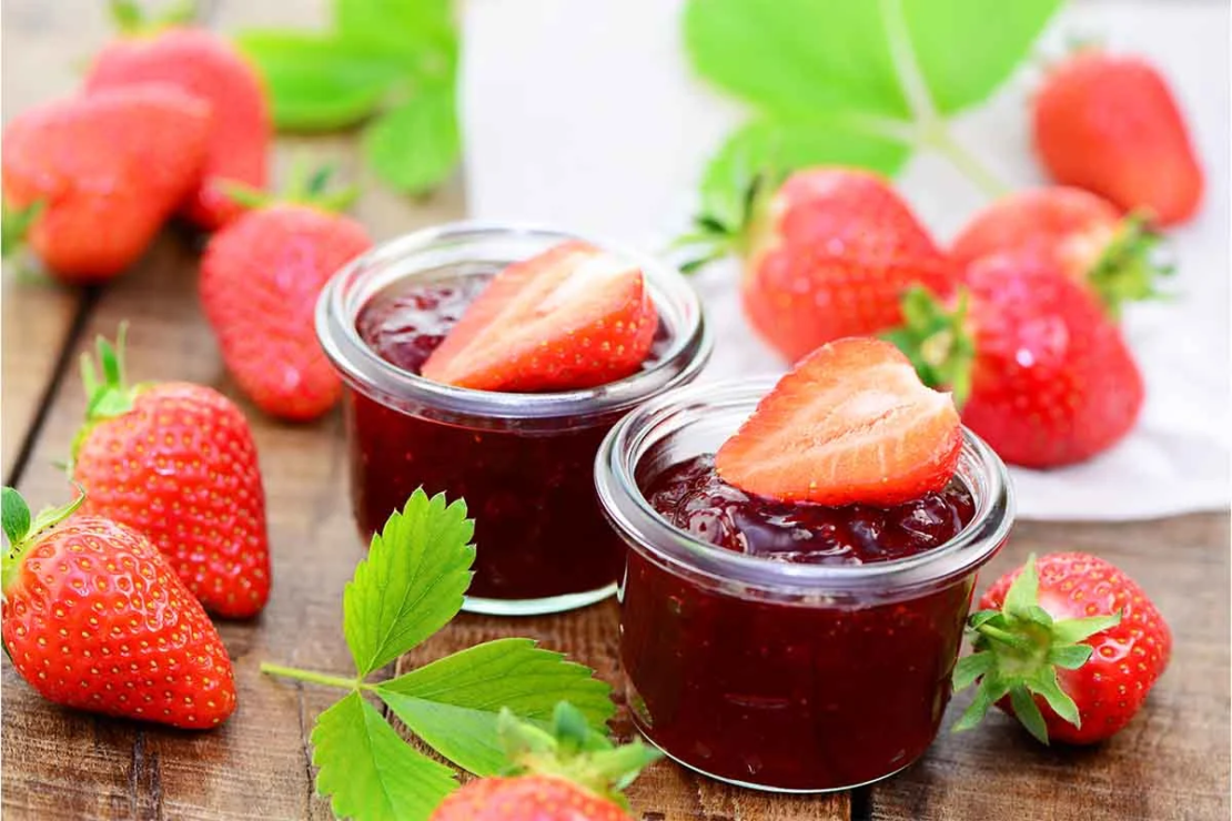 Erdbeermarmelade in Glaesern neben Erdbeeren [Foto: AdobeStock_Printemps]