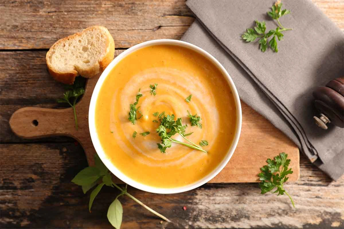 Moehrensuppe in einer Schale neben Baguettescheiben und Servietten  [Foto: AdobeStock_M.studio]