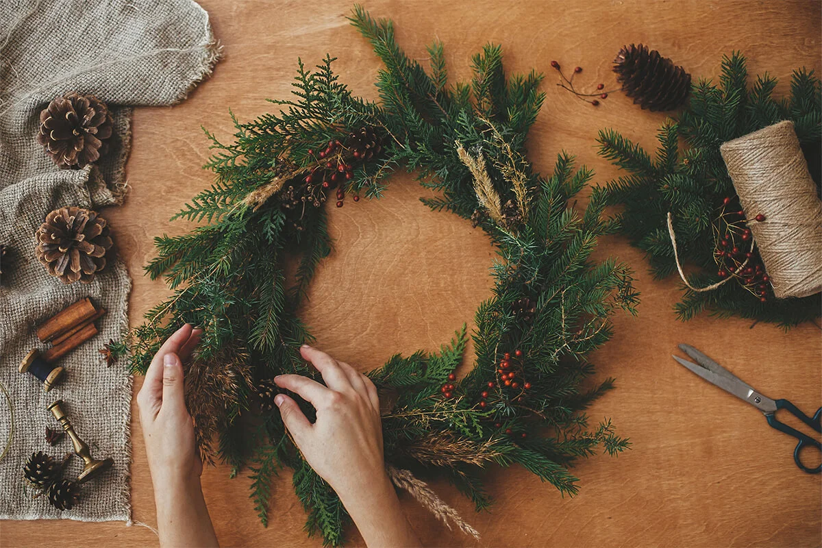 Adventskranz aus Tannenzweigen auf einem Tisch wird gebunden [Foto: AdobeStock_Sonyachny]