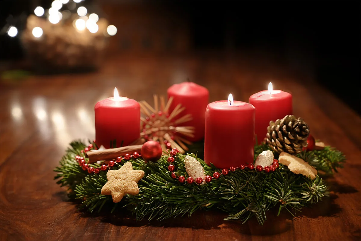 selbstgemachter Adventskranz mit roten Kerzen, Strohsternen und Gebäck verziert auf einem Holztisch [Foto: AdobeStock_Maren Winter]