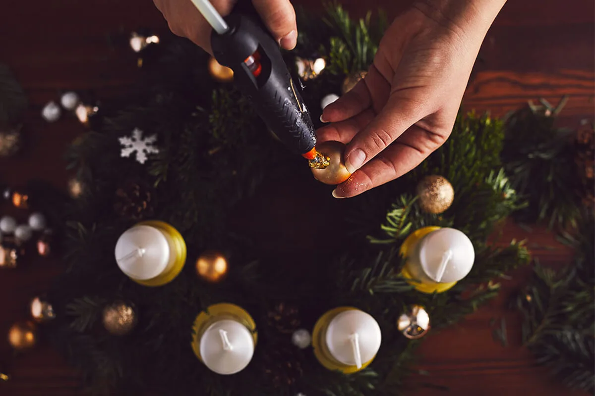 Weihnachtskugeln verschiedener Größe werden mit Heißkleber auf einem Adventskranz fixiert. [Foto: AdobeStock_Rostislav_Sedlacek]