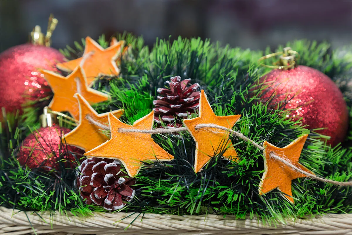 getrocknete Orangenschalen als Girlande an Adventskranz, zusätzlich sind Tannenzapfen und Kugeln zu sehen [Foto: AdobeStock_EyeEm]