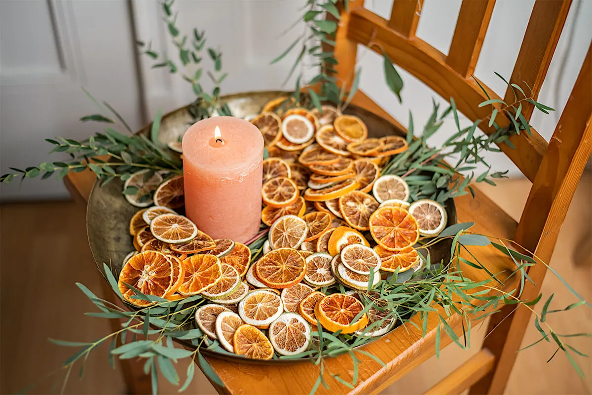 viele getrocknete Orangenschalen auf einem Tablett mit Eukalyptus und einer Kerze [Foto: AdobeStock_Knipseria]