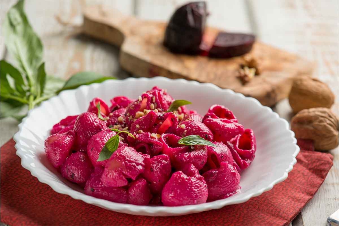 Pink Pasta mit Walnuessen auf einem weissen Porzellan-Teller, der auf einem orangefarbenen Stoffdeckchen steht. [Foto: AdobeStock_Marco Mayer]