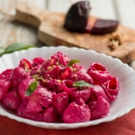 Pink Pasta mit Walnuessen auf einem weissen Porzellan-Teller, der auf einem orangefarbenen Stoffdeckchen steht. [Foto: AdobeStock_Marco Mayer]