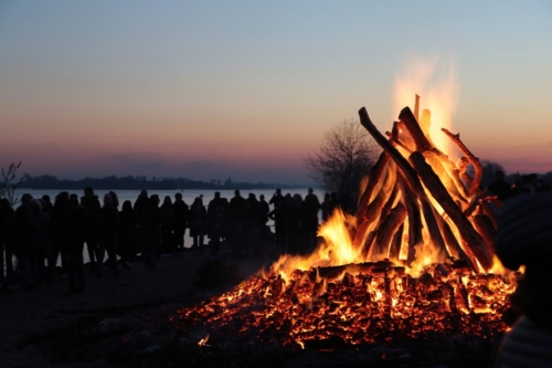 Das Osterfeuer am Strand von Hamburg-Blankenese brennt in der Dämmerung und ist umringt von einer großen Menschenschar, die im Gegenlicht nur in Umrissen zu erkenne ist