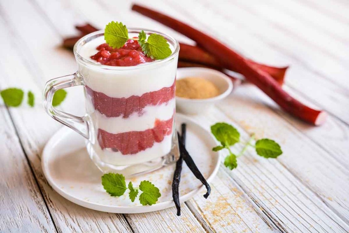 Dieses Joghurt-Rhabarber-Dessert ist ein Oster-Rezept fuer alle, die es leicht und sueß moegen. Hier in einem Glas angerichtet und auf einem Unterteller mit Vanilleschote serviert. [Foto: AdobeStock_noirchocolate]