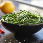 Salatschale mit Queller auf einem dunkeln Tisch mit einer Zitrone und Chili im Hintergrund [Foto: AdobeStock_Madeleine Steinbach]