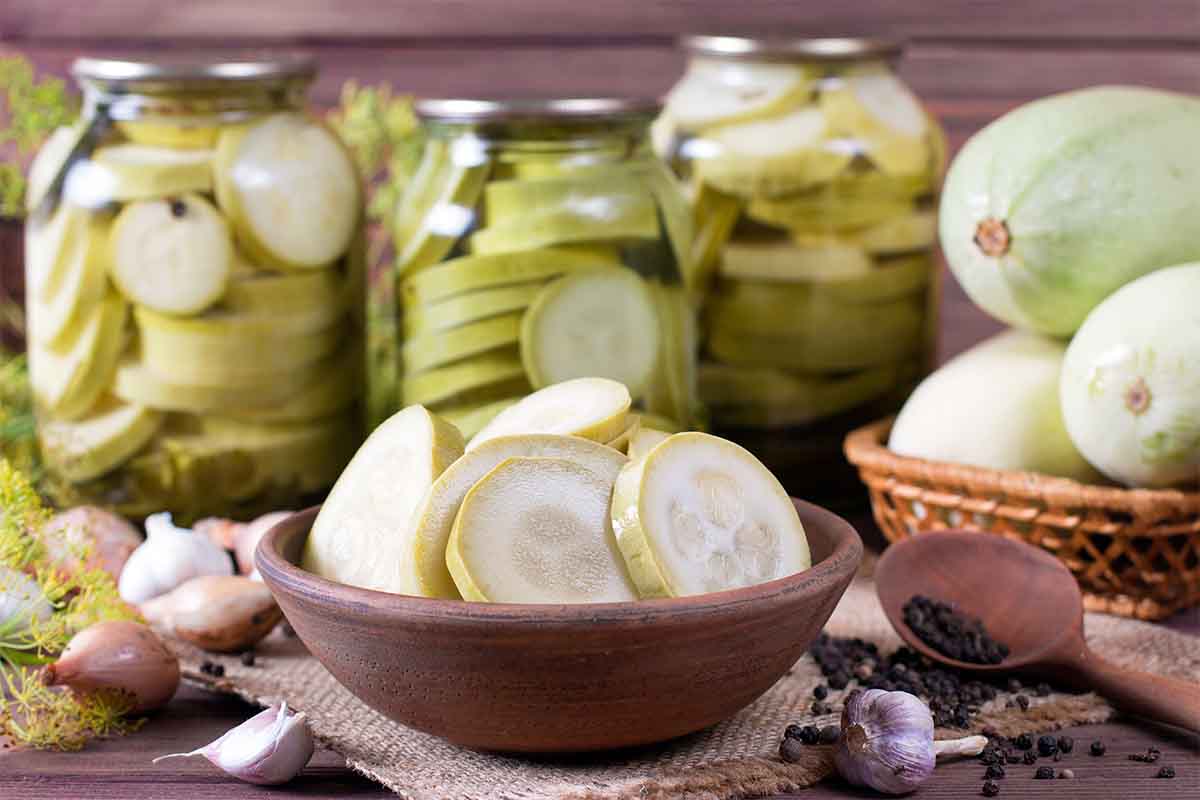 Eingelegte Zucchini in Einmachgläsern und frisch geschnittene Zucchinischeiben in einer Schüssel im Vordergrund – ideal für Zucchinisalat oder als Vorrat für den Winter. [Foto: AdobeStock_qwartm]